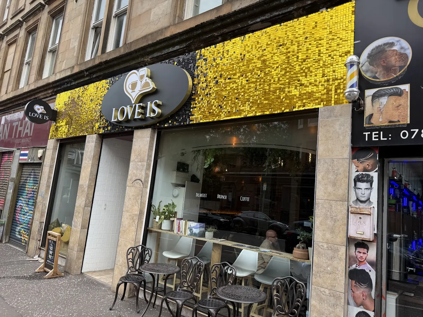 The Love Is café shopfront on Dumbarton Road, with a gold sequin fascia, dark oval sign and pavement tables outside